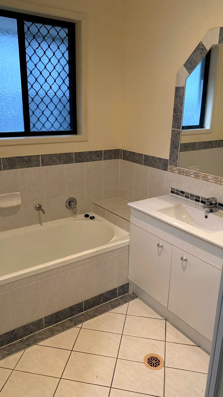 Before: dated bathroom with cream walls, burgundy-grey border tiles, an old bath and a basic vanity