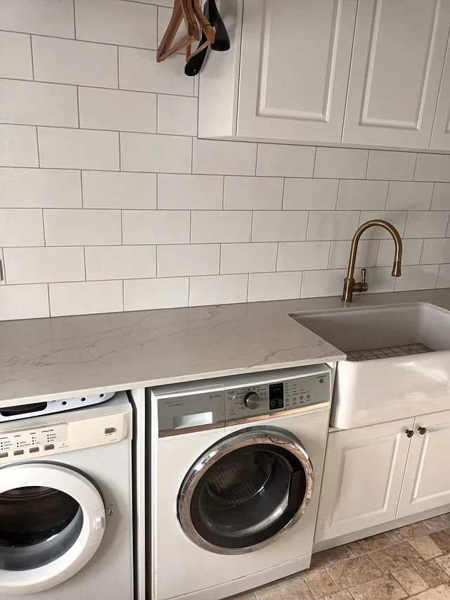 Laundry with white subway wall tiles, a brass mixer tap, farmhouse sink and front-loading washers