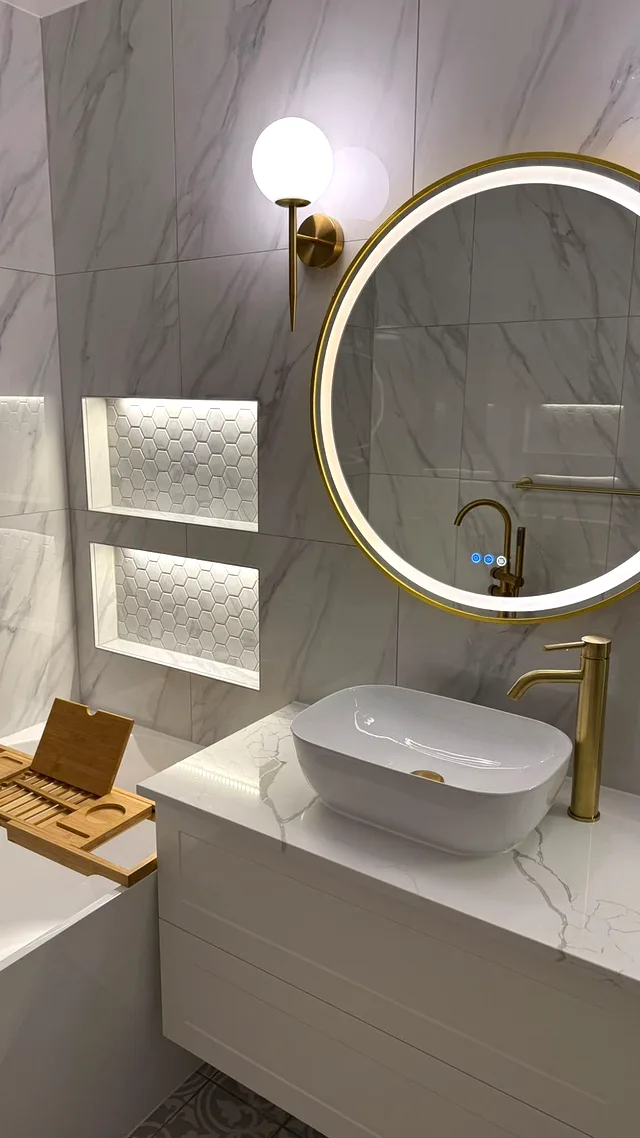 Floating white vanity with a vessel basin, brass tap, round LED mirror and hexagon-mosaic niches on marble-look tiles