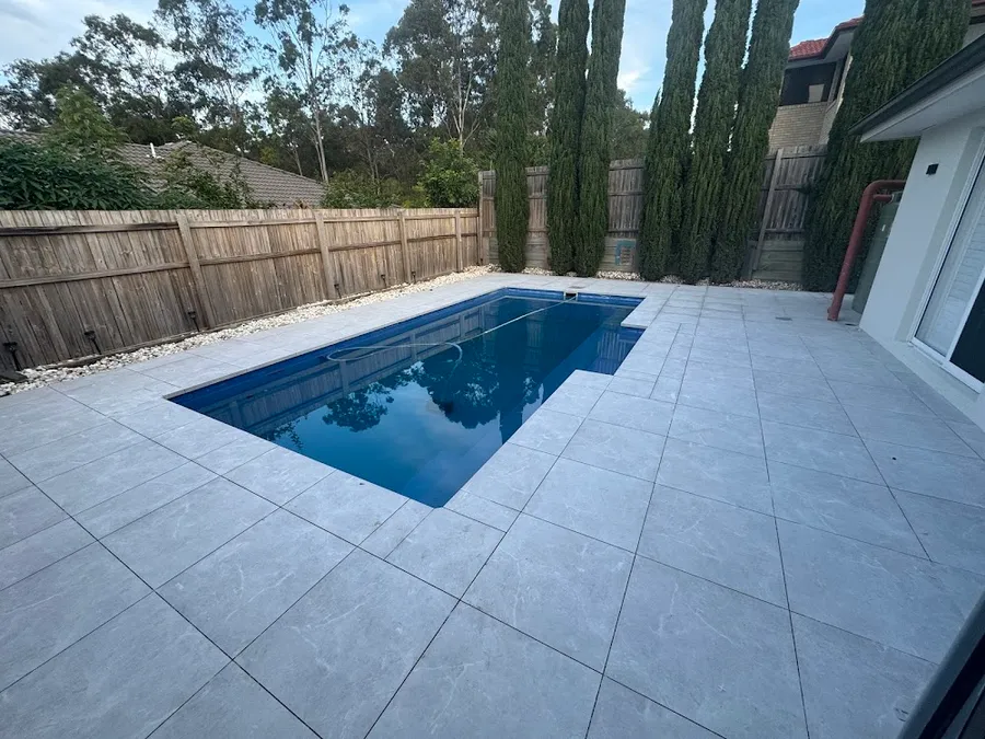 Newly tiled pool surround with a blue pool and light grey large-format tiles