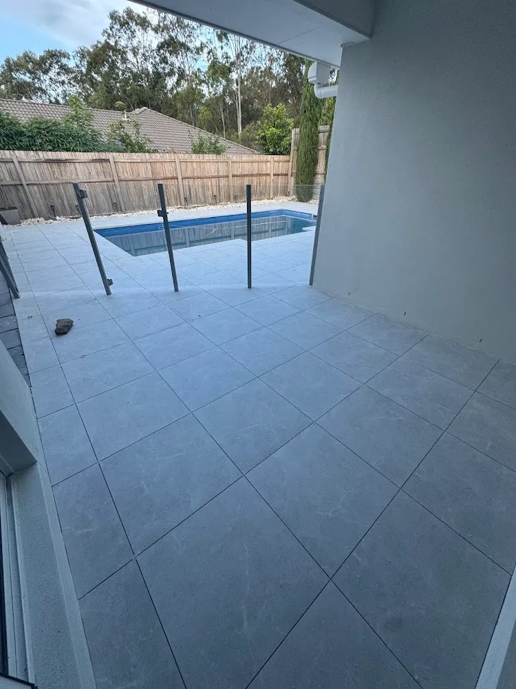 Light grey large-format tiles laid around a pool and glass fence
