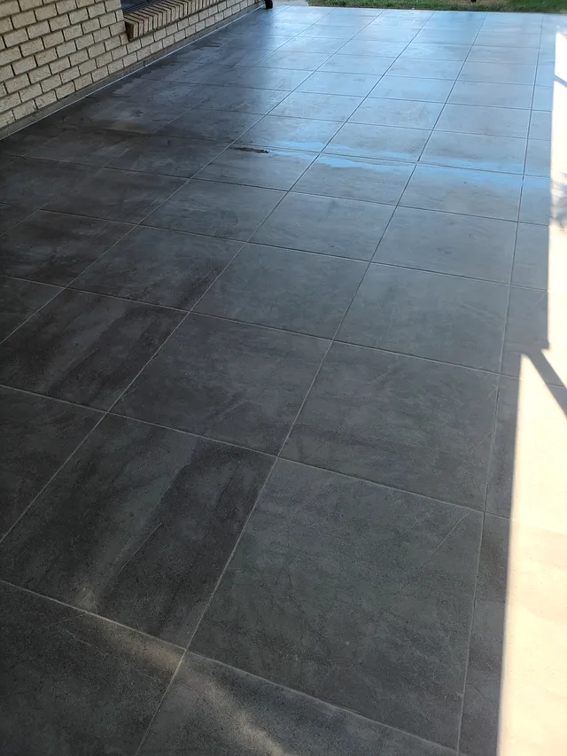 Charcoal outdoor tiles being laid with levelling clips beside a brick home