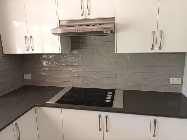 Grey glossy splashback tiles above a black cooktop with white cabinetry