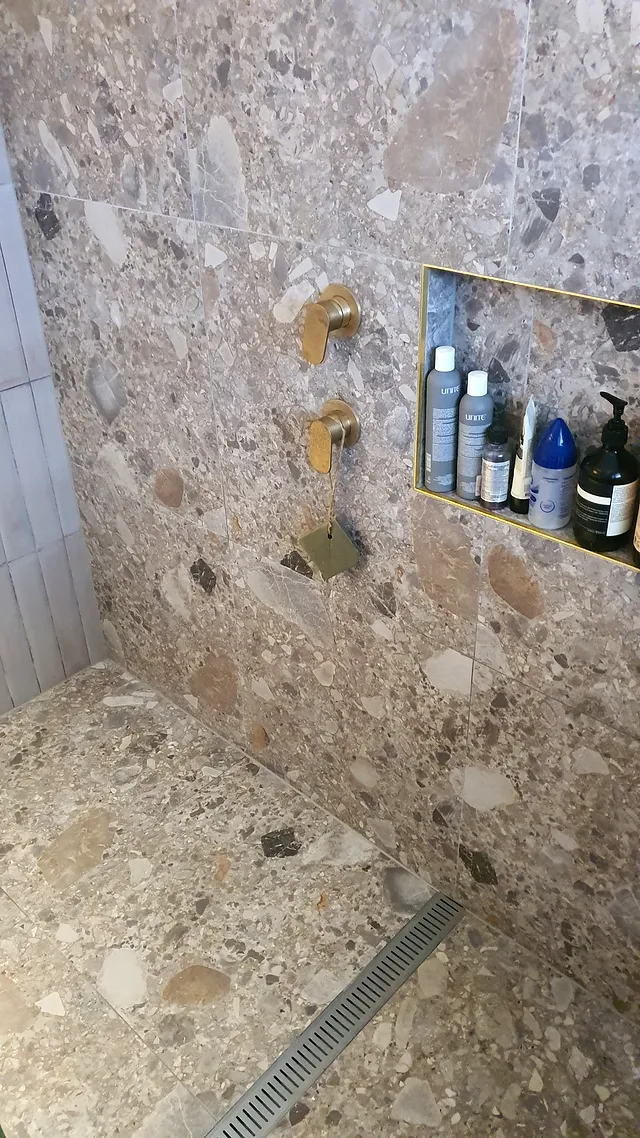 Terrazzo-look shower wall with brass tapware and a recessed shelf niche