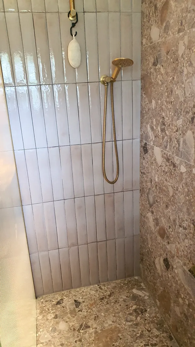 Shower with vertical stacked wall tiles, a brass shower and terrazzo feature wall